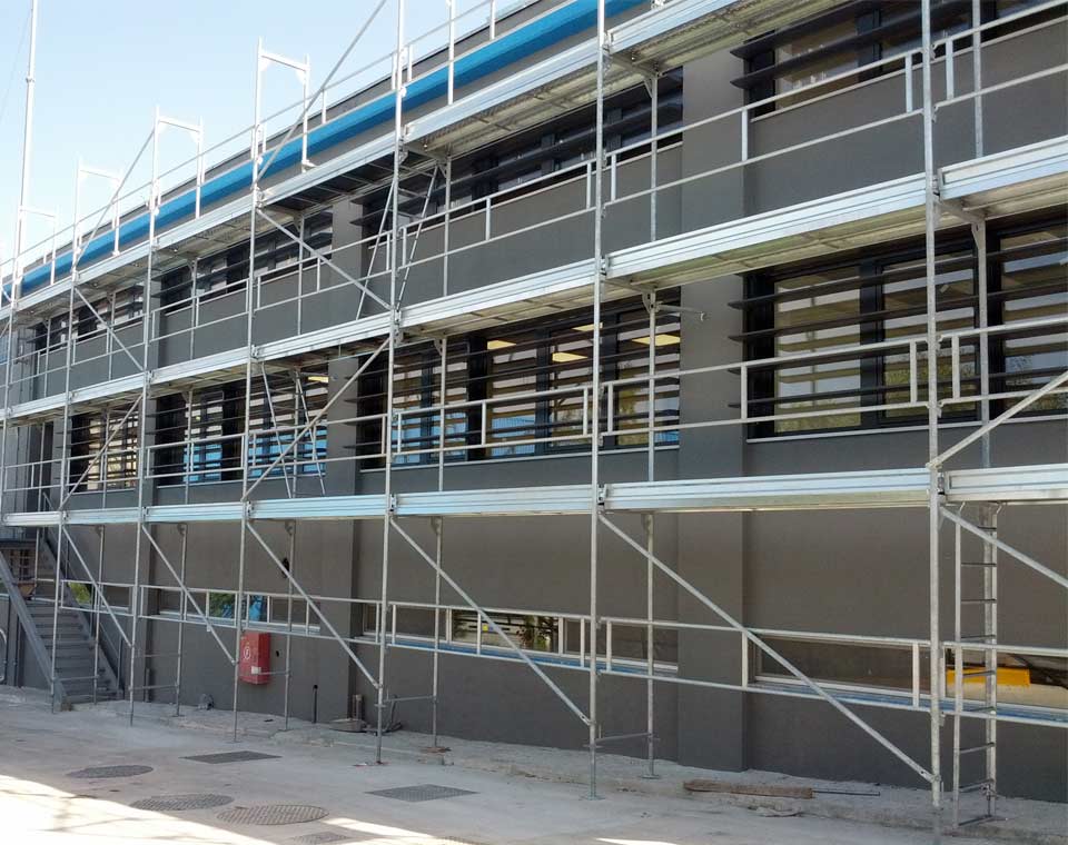 Σκαλωσιά σε σύγχρονο κτίριο με σκούρη πρόσοψη και επίπεδα εργασίας.