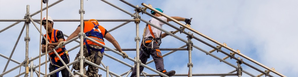 Τρεις τεχνίτες σε εκτεταμένη σκαλωσιά σε εξωτερικό έργο.